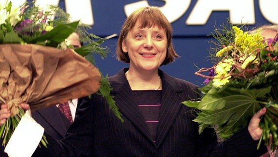 Nach ihrer Wahl zur neuen Vorsitzenden der CDU bedankt sich Angela Merkel bei den Delegierten des CDU-Bundesparteitages in Essen und winkt mit zwei Blumensträußen. © picture-alliance/dpa Foto: Michael Jung