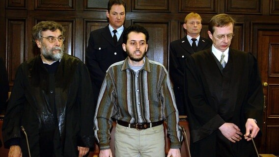 Der Angeklagte Mounir Al-Motassadeq steht vor der Urteilverkündung am 19. Februar 2003 im Verhandlungssaal des Landgerichts in Hamburg zwischen seinen Verteidigern Hartmut Jacobi (l) und Hans Leistritz (r). Er wurde im weltweit ersten Prozess um die Terroranschläge vom 11. September 2001 zu 15 Jahren Haft verurteilt. © picture-alliance / dpa | DB Hansen 