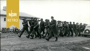 Mit einem Lied marschiert eine Gruppe des Bundesgrenzschutzes vorbei an einer der ersten fertigen Hütten, 1954 © IMAGO / ZUMA Wire 