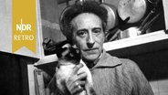 Jean Cocteau mit einer Katze auf dem Arm in einer Küche. © IMAGO IMAGES / United Archives International 