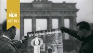 Zwei Männer halten ein Plakat des „Kuratorium Unteilbares Deutschland“ vor das Brandenburger Tor in Berlin. Auf dem Plakat ist der Schriftzug „Wir bleiben zusammen“ abgebildet. November 1961 © IMAGO / ZUMA/Keystone 