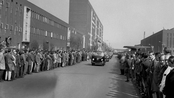 VW-Beschäftigte säumen 1968 einen Weg auf dem Werksgelände, als ein Pritschenwagen mit dem Sarg des verstorbenen Vorsitzenden Heinrich Nordhoff vorbeifährt. © Volkswagen AG 