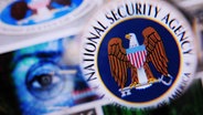 Illustration:  Durch eine Lupe ist das Logo des US-Geheimdienstes National Security Agency (NSA) auf einem Monitor zu sehen. © picture alliance / dpa Foto: Nicolas Armer
