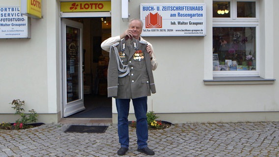 Der ehemalige NVA-Major Walter Graupner mit einer alten Uniform vor seinem Buchladen in Eggesin. © NDR 