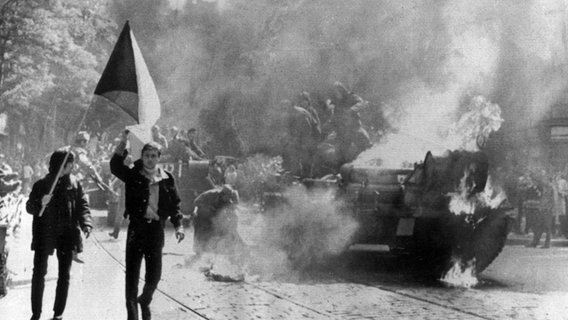 Demonstranten mit der tschechischen Flagge laufen am 21. August 1968 in Prag neben einem brennenden sowjetischen Panzer. © picture-alliance/ dpa | UPI 