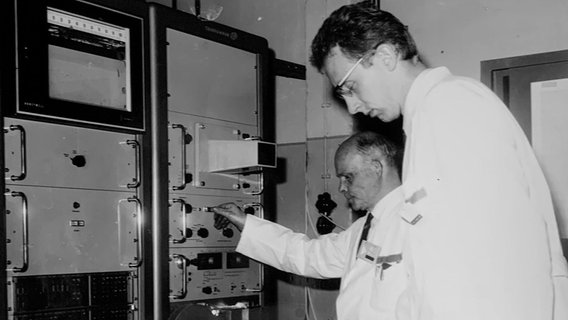 Kernphysiker Hans-Georg Priesmeyer und ein Kollege bei der Arbeit an einer Anlage, undatierte Schwarz-Weiß-Aufnahme. © privat 