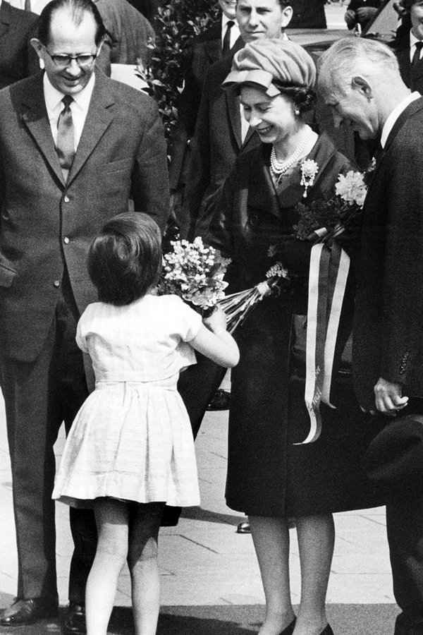 Ein kleines Mädchen überreicht Königin Elizabeth II. beim Verlassen des Bahnhofs Dammtor in Hamburg am 28. Mai 1965 einen Blumenstrauß. Links ein Dolmetscher, rechts Bürgermeister Paul Nevermann. © picture alliance / dpa 