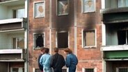Jugendliche stehen am 25. August 1992 vor dem brandzerstörten Asylbewerberheim in Rostock-Lichtenhagen. © picture alliance / ZB Foto: Bernd Wüstneck