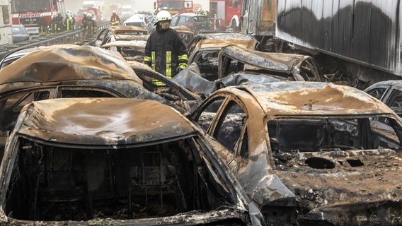 Feuerwehrleute stehen zwischen verbrannten Autowracks © dpa Foto: Bernd Wüstneck