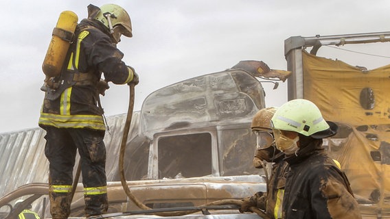 Feuerwehrleute mit Atemschutzmasken bei einem Löscheinsatz vor ausgebrannten Fahrzeugen © picture alliance / dpa Foto: Bernd Wüstneck