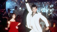 John Travolta und Karen Lynn Gorney tanzen in dem Film "Saturday Night Fever" in einer Disco. © picture alliance/Mary Evans Picture Library 