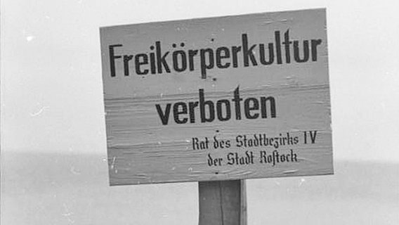 Ein Schild mit der Aufschrift "Freikörperkultur verboten" am Strand von Warnemünde im Jahr 1953. © Bundesarchiv / CC-BY-SA (http://creativecommons.org/licenses/by-sa/3.0/de/deed.de) 