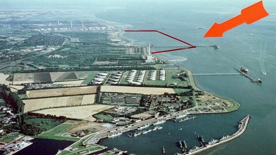 Der Marinehafen (vorne) und der Ölhafen (r.) von Wilhelmshaven an der Jademündung (Archivbild vom Sommer 1999). Der rote Pfeil auf dem Foto deutet auf ein rot markiertes Areal, in dem der neue JadeWeserPort als einziger deutscher Tiefwasserhafen entstehen soll. © picture-alliance / dpa/dpaweb Foto: Klaus_Schreiber