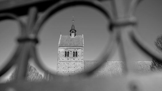 Die historische St.-Johannes-Kirche am Marktplatz im Ortskern von Bad Zwischenahn, fotografiert durch ein gusseisernes Zaunelement. © picture alliance/dpa Foto: Hauke-Christian Dittrich