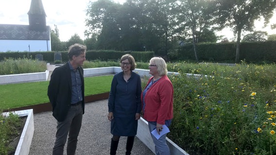 Pastor Hans-Joachim Stuck, die Leiterin der Gedenkstätte Katja Happe und Gudrun Jessen-Hansen im Garten der Begegnung der KZ-Gedenkstätte Ladelund © NDR Foto: Michael Hollenbach