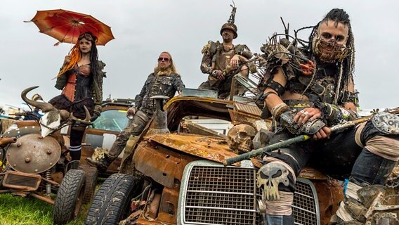 Franzi, Sean, Kai und Joris (v.l.n.r.) von den Wasteland Warriors sitzen am 4. August 2017 in Wacken (Schleswig-Holstein) auf dem Festivalgelände des Wacken Open Air auf Autos, die im "Mad Max"-Stil umgebaut wurden. © picture alliance / Christophe Gateau/dpa | Foto: Christophe Gateau