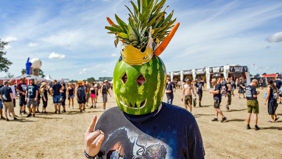 01.08.2018, Wacken: Ein Festivalbesucher hat sich einen Helm aus einer Wassermelone, zwei Mohrrüben und einer Ananas gebastelt. © picture alliance/dpa Foto: Axel Heimken