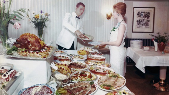 Eine Passagierin wird auf der "Cap San Diego" von einem Kellner am Buffet bedient (Aufnahme aus den 1960er-Jahren). © Hamburg Süd 