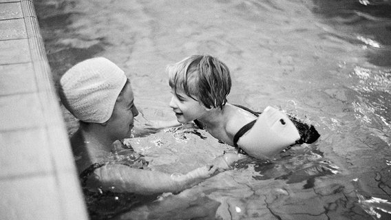 Eine Frau hilft einem jungen Mädchen mit Schwimmflügeln in den 70er-Jahren beim Schwimmen. © picture alliance / United Archives Foto: Werner Otto