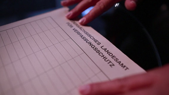 Eine Hand legt ein Formular des Niedersächsischen Landesamts für Verfassungsschutz auf einen Tisch. © NDR 