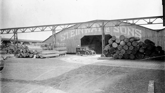 Gestapelte Baumstämme und ein Auto vor dem Holzlager der Firma Steinway & Sons im Hamburger Rondenbarg, undatierte Aufnahme. © Steinway & Sons 