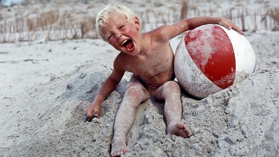 DDR-Werbeaufnahme: Ein Kleinkind sitzt fröhlich am Strand von Hiddensee (29.07.1966) © picture alliance / Caro Foto: Sorge