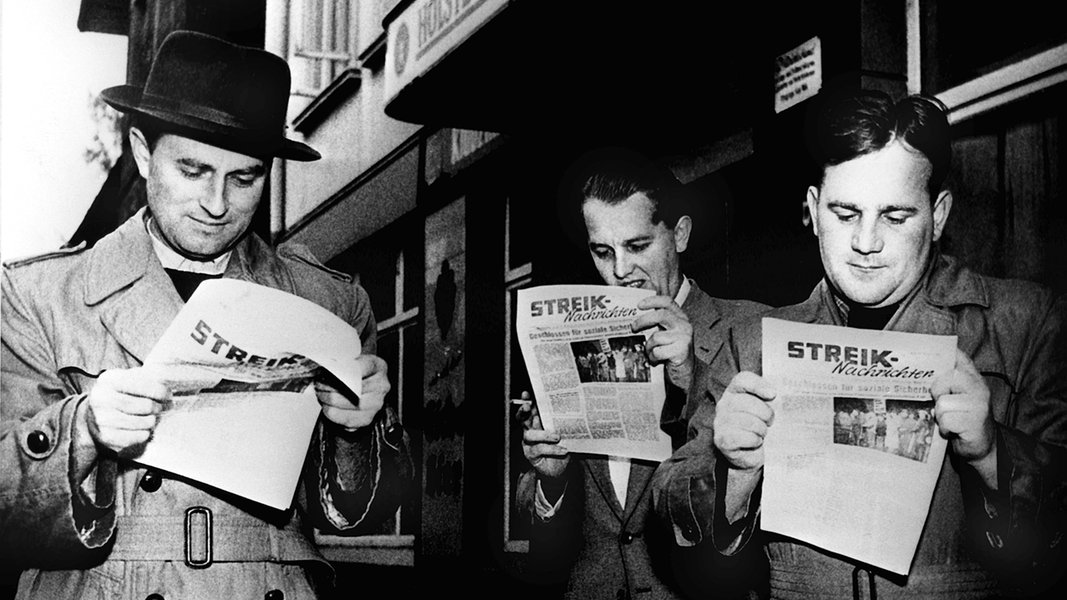 Streikende Arbeiter in Kiel lesen am 25. Oktober 1956, dem zweiten Streiktag, die neue vierseitige Streikzeitung.