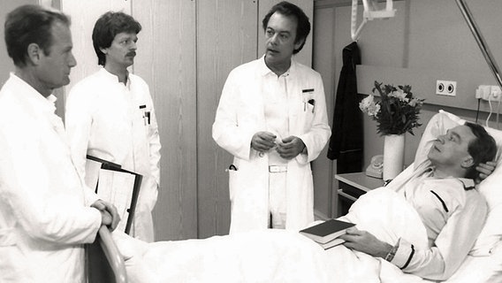 Drei Ärzte stehen am Bett eines Patienten (Szene aus der Fernsehserie Schwarzwaldklinik von 1984). © Studio Hamburg/NDR 