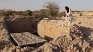 Ein Mausoleumsverwalter betet 2014 an einem beschädigten Grab in Timbuktu (Mali). Im westafrikanischen Mali überrannten radikale Islamisten 2012 Timbuktu, die historische Stadt der islamischen Kultur. Die Militanten zerstörten 14 der 16 Gräber prominenter Persönlichkeiten der Stadt. © picture alliance / AP Photo Foto: Baba Ahmed
