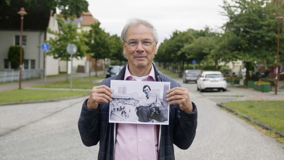 Fotoreporter Harald Schmitt hält ein altes Foto von sich in Ost-Berlin in den Händen. © NDR /jumpmedientv GmbH Foto: -