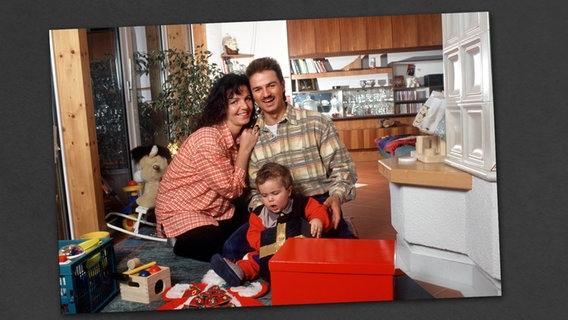 Ein Vater und eine Mutter sitzen hinter ihrem Sohn, der Geschenke auspackt. © picture-alliance 