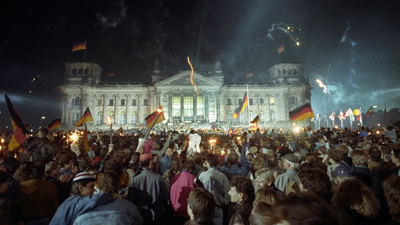Menschen feiern in der Nacht zum 3. Oktober 1990 mit Deutschlandfahnen und Feuerwerk vor dem Berliner Reichstag die deutsche Wiedervereinigung. © picture-alliance/ dpa Foto: Jörg Schmitt
