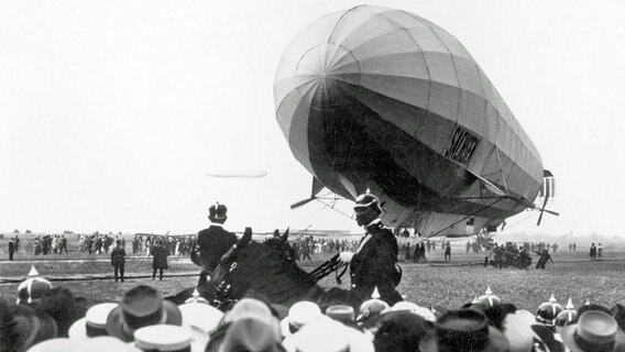 Menschen beobachten um 1915 die Landung eines Zeppelins auf einer Wiese. © picture-alliance / IMAGNO/Austrian Archives 
