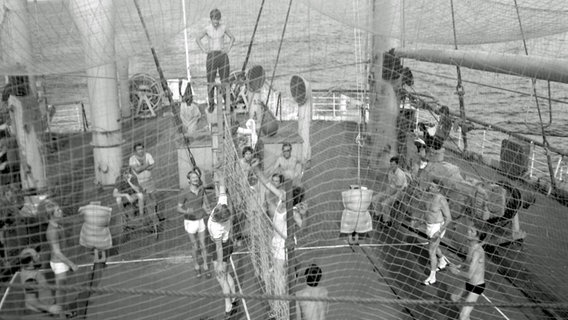 Seeleute und das Drehteam der Serie "Zur See" spielen an Bord des Schiffes "Fichte" in einem eingezäunten Feld Volleyball. © Stiftung Deutsches Rundfunkarchiv 