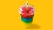 Bunter Slushie in Regenbogenfarben in einem Plastikbecher mit grün-weißen Trinkhalm. © Photocase Foto: etorres69