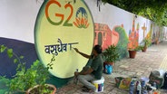 G20 Gipfel in Neu Delhi, ein Mann malt das G20-Logo mit Lotusblüte auf eine weiße Mauer © NDR/Peter Hornung Foto: Peter Hornung