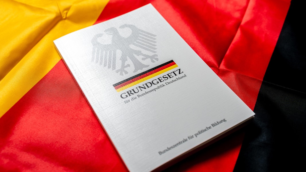 Ein Grundgesetz der Bundesrepublik Deutschland liegt auf einer deutschen Flagge. 
