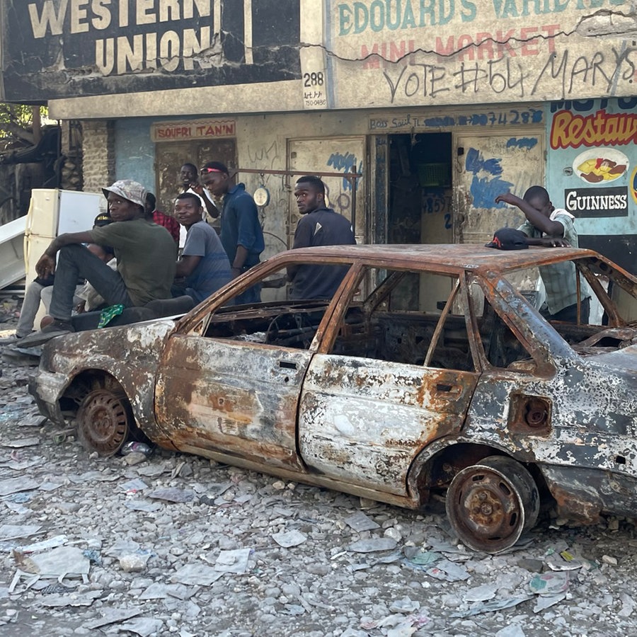 Jugendliche sitzen auf einem ausgebranntem Auto im Stadtteil Carrefour-Feuilles auf Haiti © NDR Foto: Anne Demmer