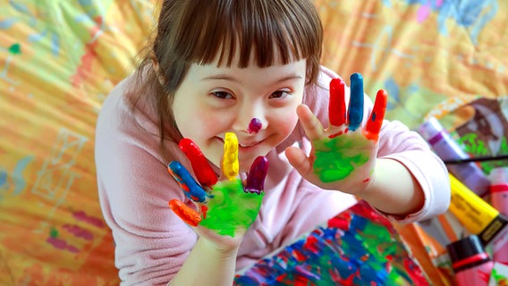 Ein kleines Mädchen hält lachend ihre Hände hoch, diese sind mit Fingerfarben bunt bemalt. © Panthermedia Foto: DenysKuvaiev