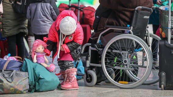 Ein Mädchen spielt mit einer Puppe, im Hintergrund ist ein Rollstuhl zu sehen. © Picture Alliance//dpa/dpa-Zentralbild Foto: Jan Woitas