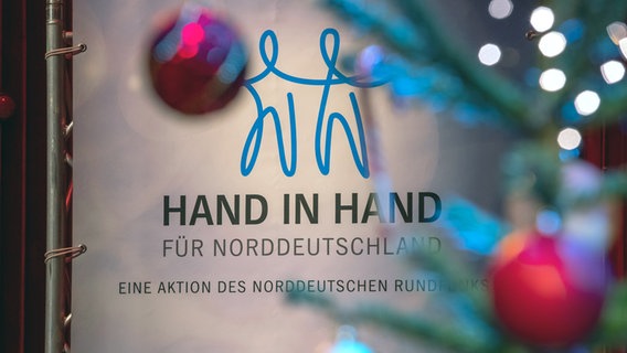 Weihnachtsbaum kugeln hängen vor einem Schild der Spendenaktion "Hand in Hand in Norddeutschland". © NDR Foto: Axel Herzig
