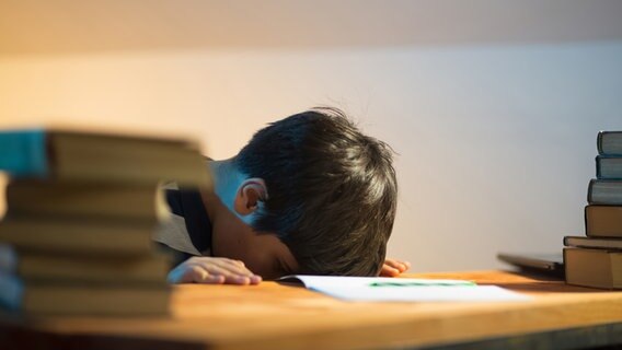 Ein kleiner Junge legt erschöpft seinen Kopf auf einen Tisch mit Büchern. © Photocase Foto: Sure_Production