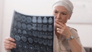 Eine Frau mit einem Kopftuch schaut nachdenklich auf eine Computertomographie eines Schädels. © PantherMedia Foto: ArturVerkhovetskiy