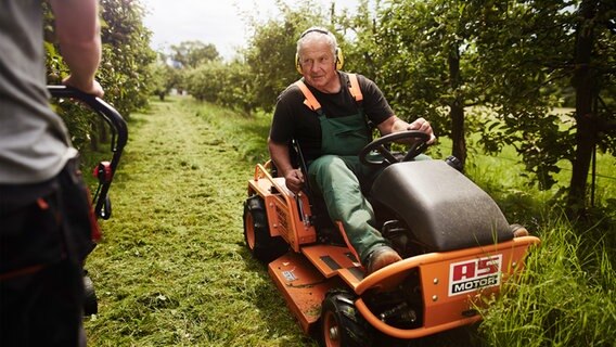 Ein Mann mit Gehörschutz sitzt auf einem Aufsitzmäher auf einem Feld. © Lebenshilfe Foto: David Maurer