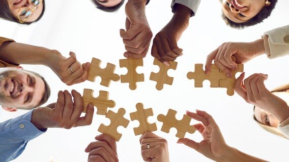 Menschen halten Puzzleteile aus Holz gegeneinander. © Colourbox 