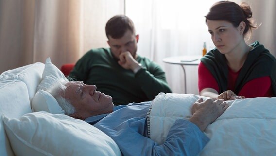 Zwei trauernde junge Menschen sitzen am Bett eines alten Mannes. © PantherMedia Foto: photographee.eu