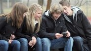 Junge Menschen sitzen auf einer Bank im Park und schauen in ein Handy © picture alliance Foto: Armin Weigel