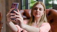 Ein Mädchen sitzt in einem Wohnzimmer, schaut in ihr Handy und nimmt sich offenbar selbst auf. © Retoncy Foto: Retoncy