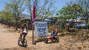 Eine Frau fährt Fahrrad auf Hawaii, neben ihr ein Protestschild mit dem Text: "Toursit keep out" © AP/Jae C. Hong Foto: Jae C. Hong