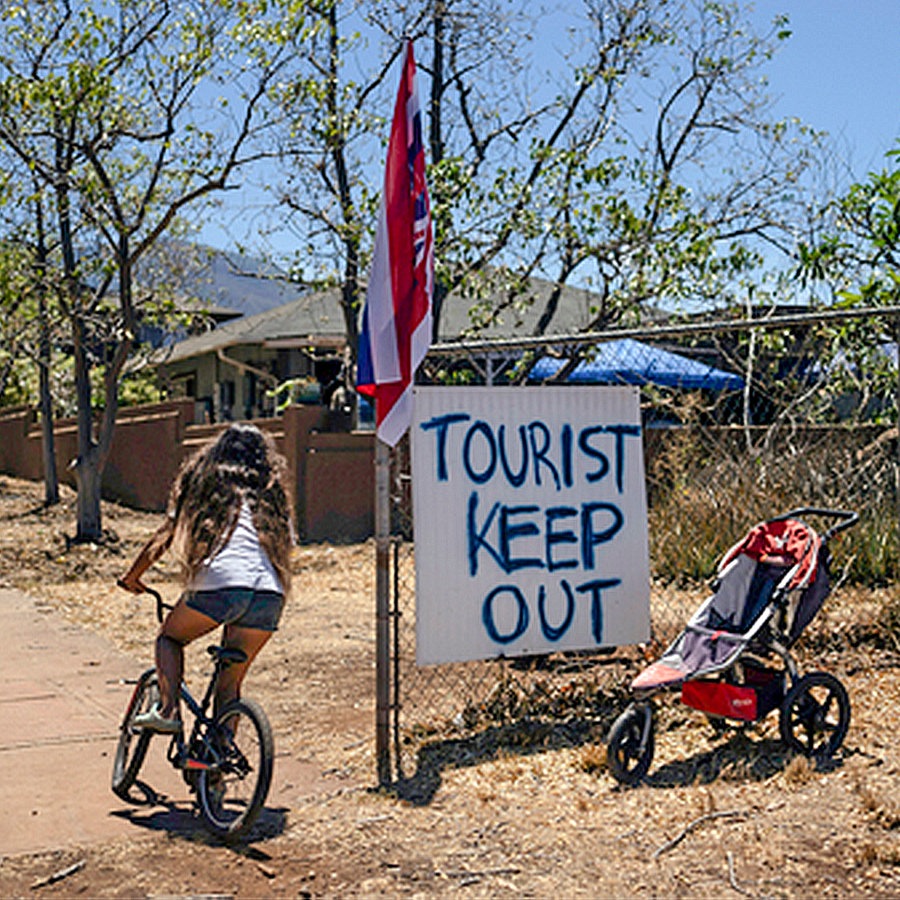 Eine Frau fährt Fahrrad auf Hawaii, neben ihr ein Protestschild mit dem Text: "Toursit keep out" © AP/Jae C. Hong Foto: Jae C. Hong